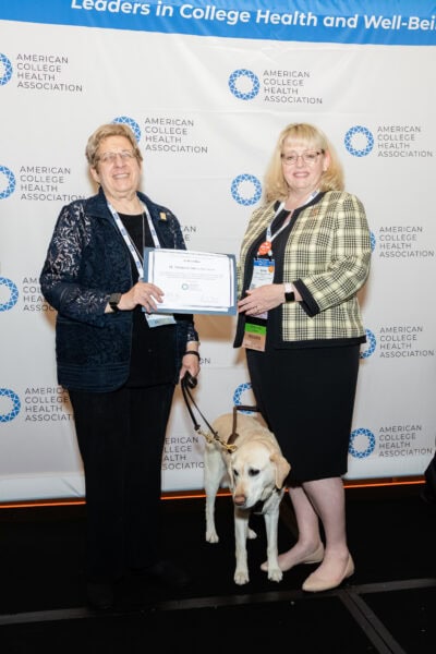 Two people with a service dog holding an award certificate