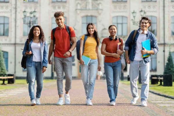 A group of smiling college students walking outside in front of a building