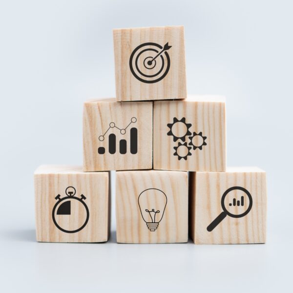 Stacked wooden blocks with various icons: a target, data graph, gears, a stopwatch, a lightbulb, and a magnifying glass