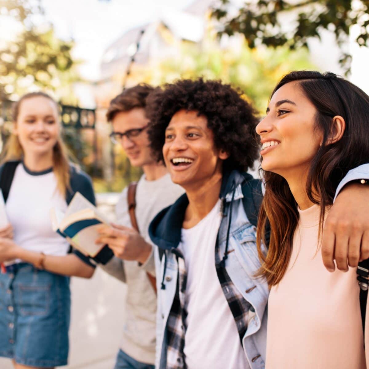 A smiling group of diverse college students walking outside with arms around each other