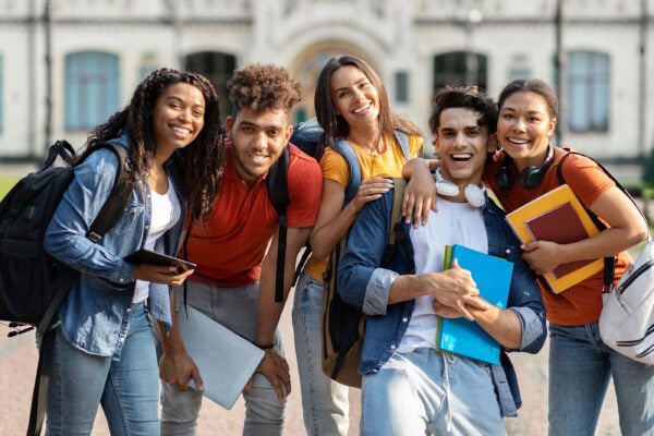 A diverse group of smiling college students outside with their backpacks and school books
