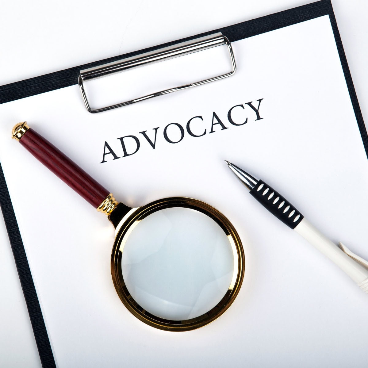 A clipboard featuring a sheet of paper that says advocacy, with pen and a magnifying glass on top