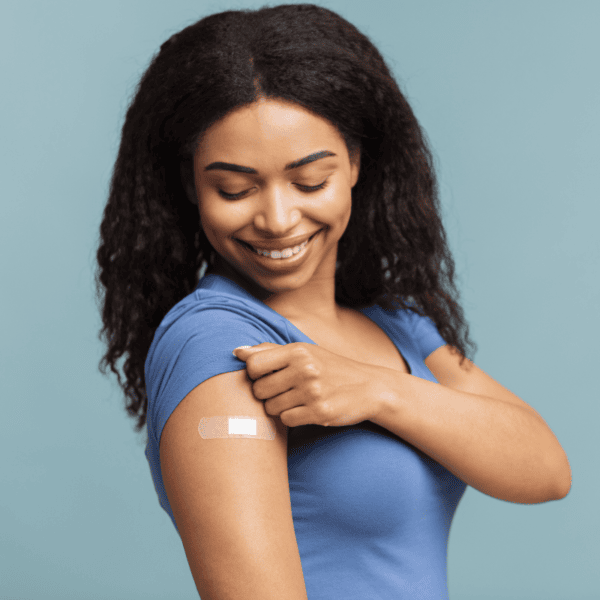 A smiling young woman pulling up her sleeve to reveal a bandage, indicating receiving a vaccination
