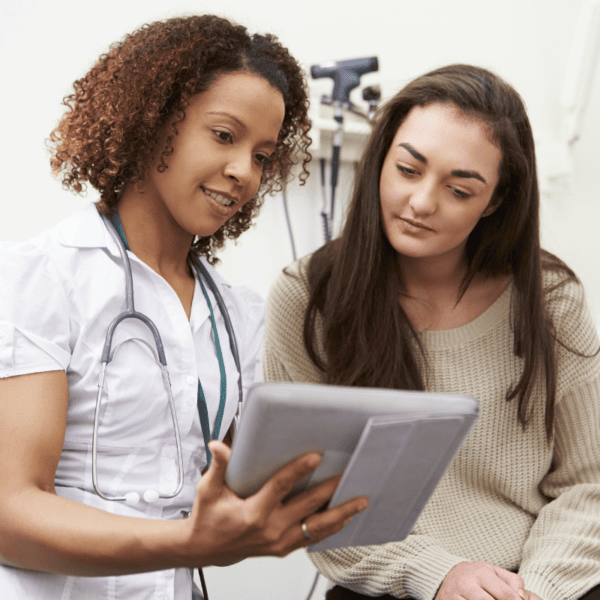A curly-haired medical professional showing a young female patient something on her tablet