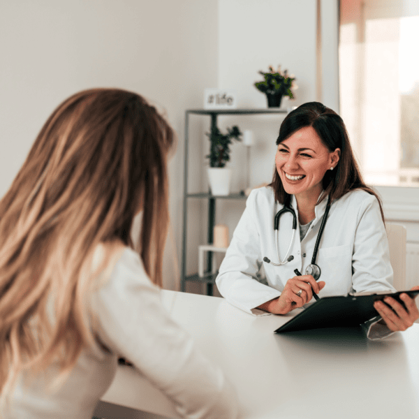 A smiling doctor holding a clipboard and talking to patient