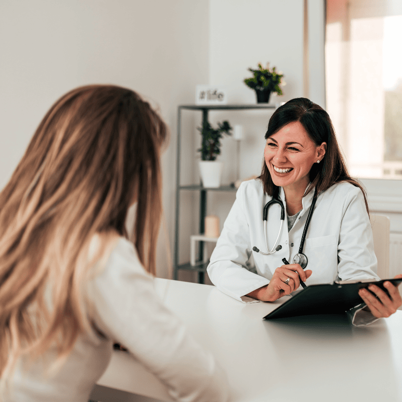 A smiling doctor holding a clipboard and talking to patient
