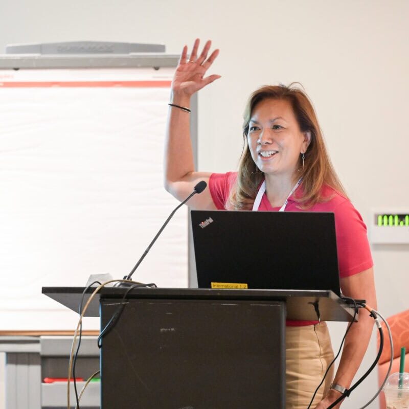 A speaker at the ACHA 2024 Annual meeting standing at a podium and raising her hand
