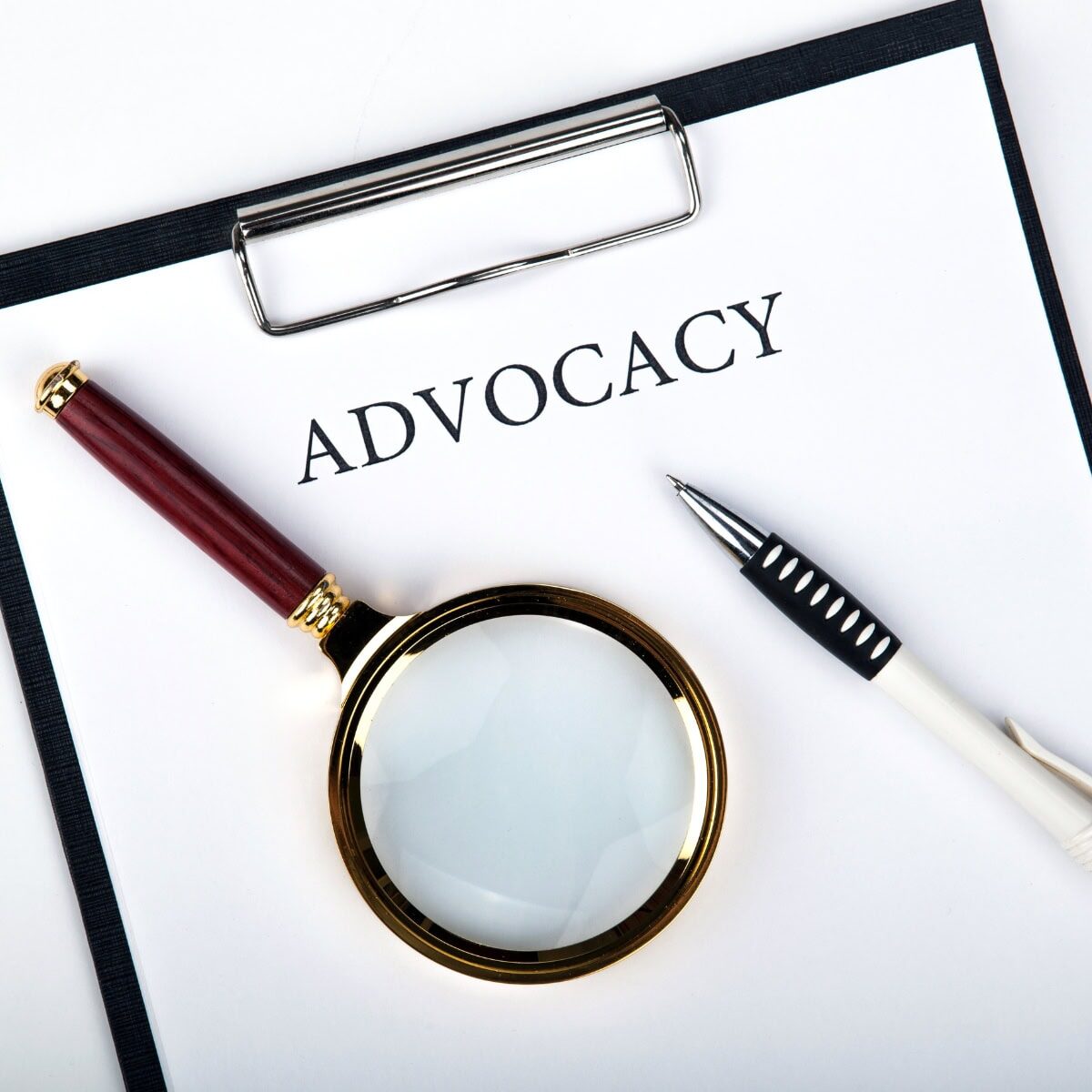 A clipboard featuring a sheet of paper that says advocacy, with pen and a magnifying glass on top