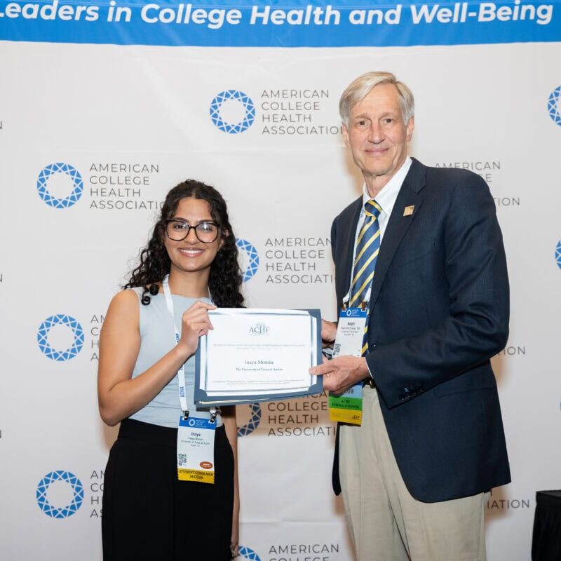Two smiling professionals posing for a photo while holding an award certificate