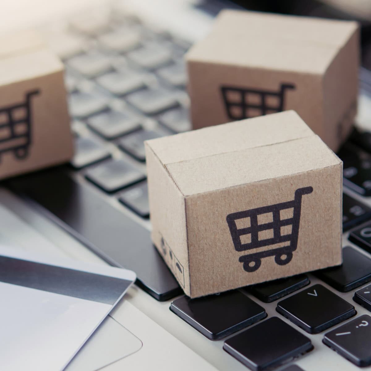 A credit card and wooden blocks with shopping cart icons sitting on top of a laptop keyboard