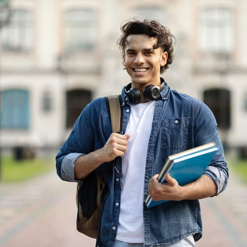 Portrait of happy handsome student guy with backpack and workbooks posing outdoors