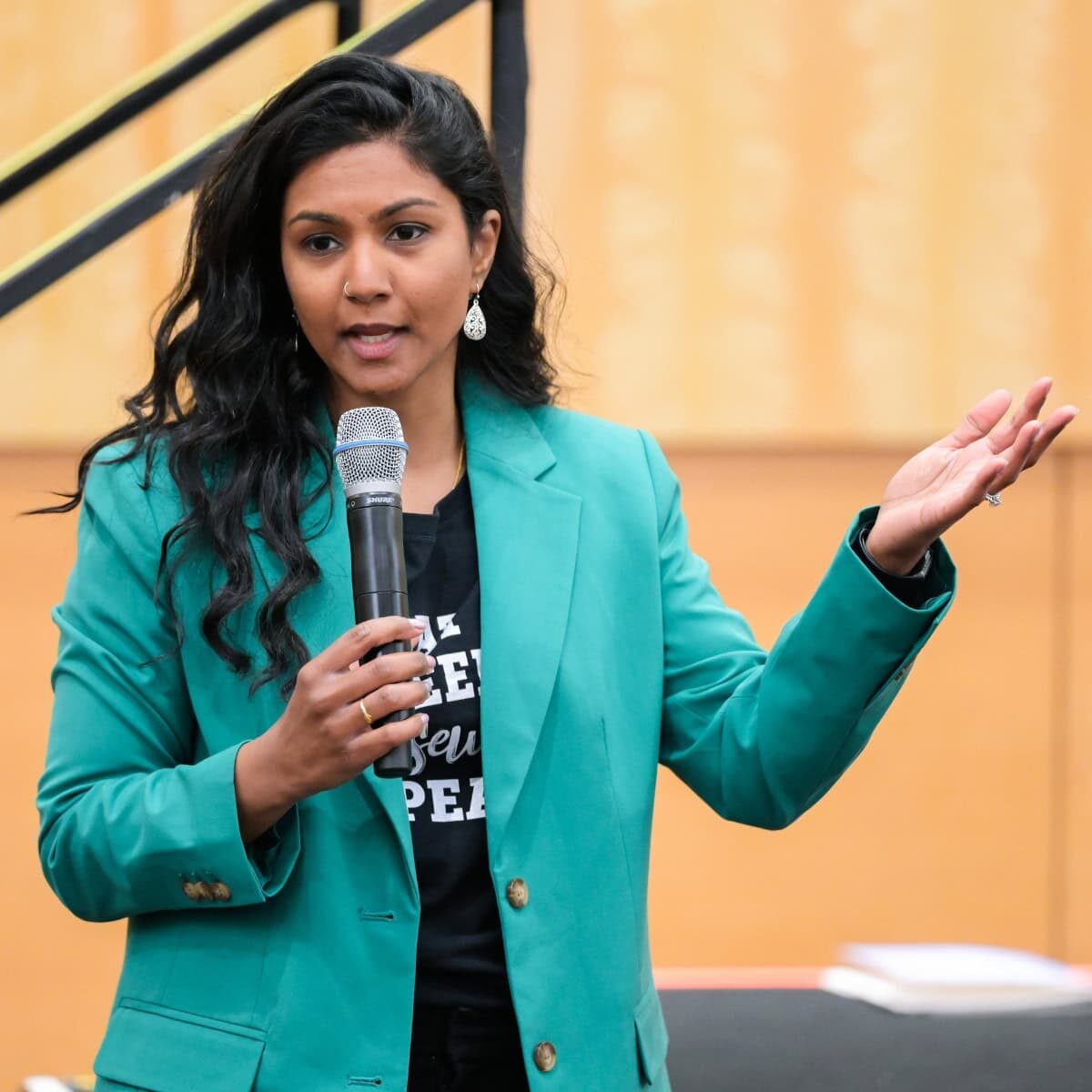 A woman in a green jacket holding a microphone and speaking at a conference