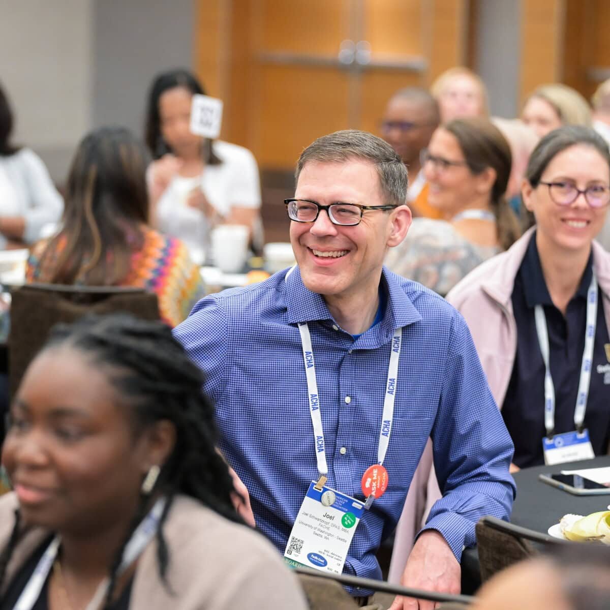 A smiling conference attendee sitting at a table with other attendees