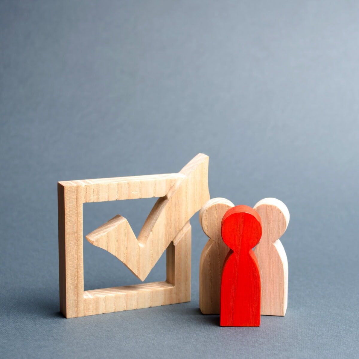 A wooden checkbox along with three wooden people shapes, one being red