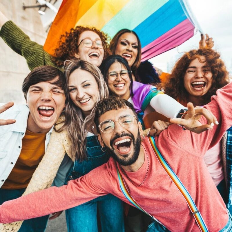 Group of LGBTQ young adults outside waving a rainbow flag