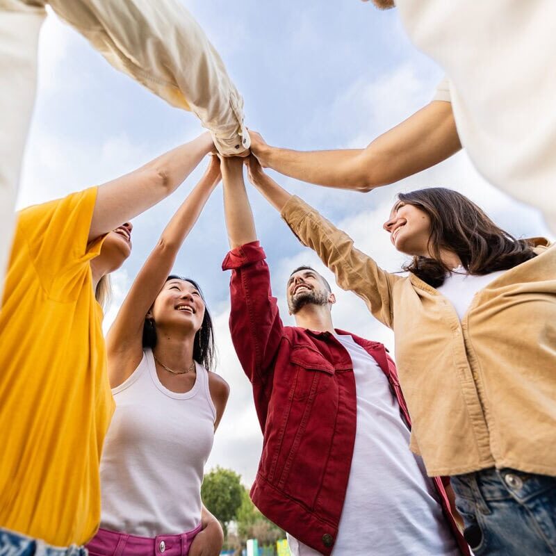 A group of students gathered together outside and putting their hands together in a circle