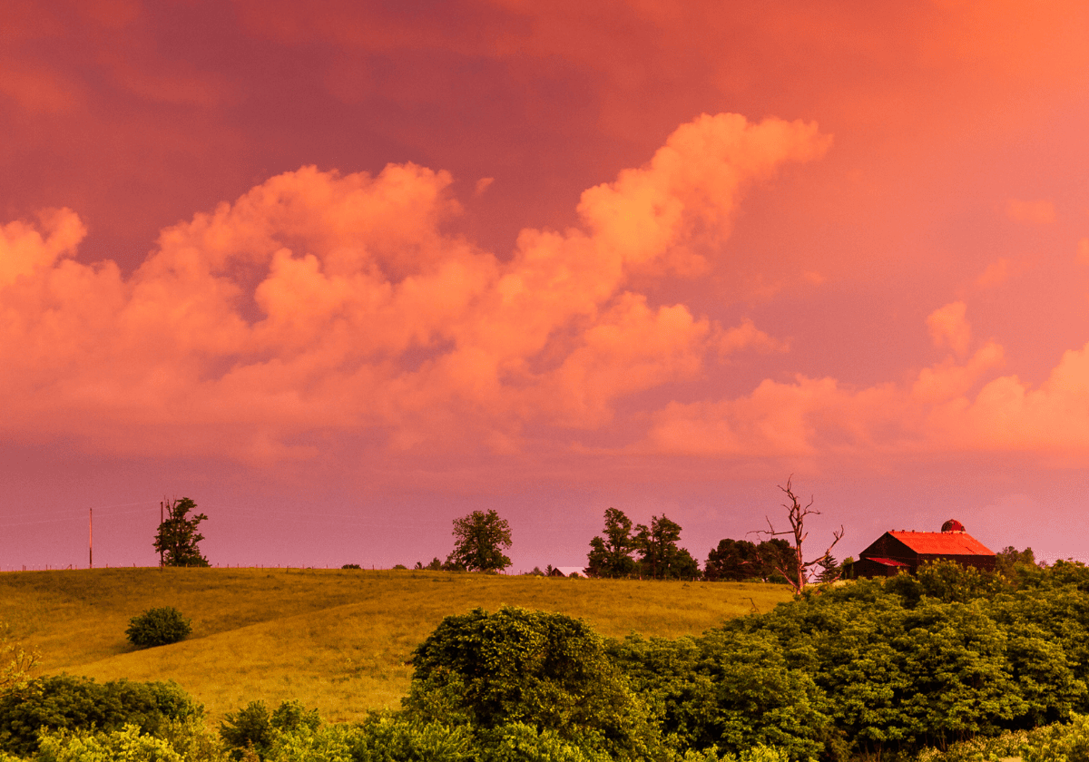 Kentucky Countryside - hills and trees with a red barn in the background and a warm colors in the sky with clouds, indicating a sunset