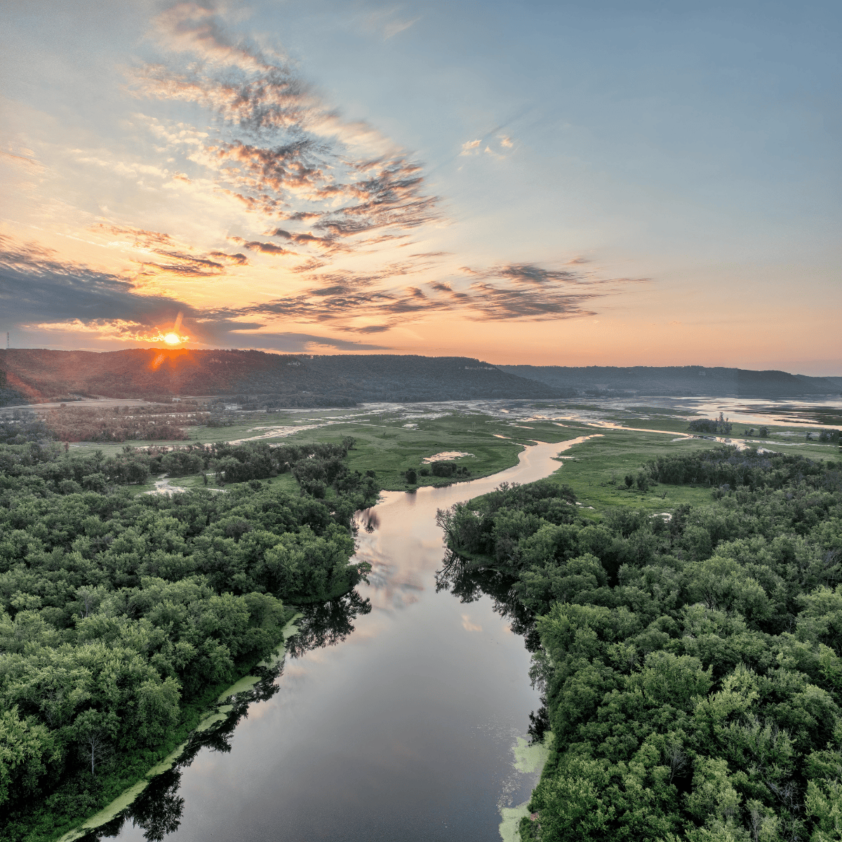 Scenic Sunrise Over Mississippi River in Minnesota - aerial view of a winding river between many trees, with a sunrise in the background