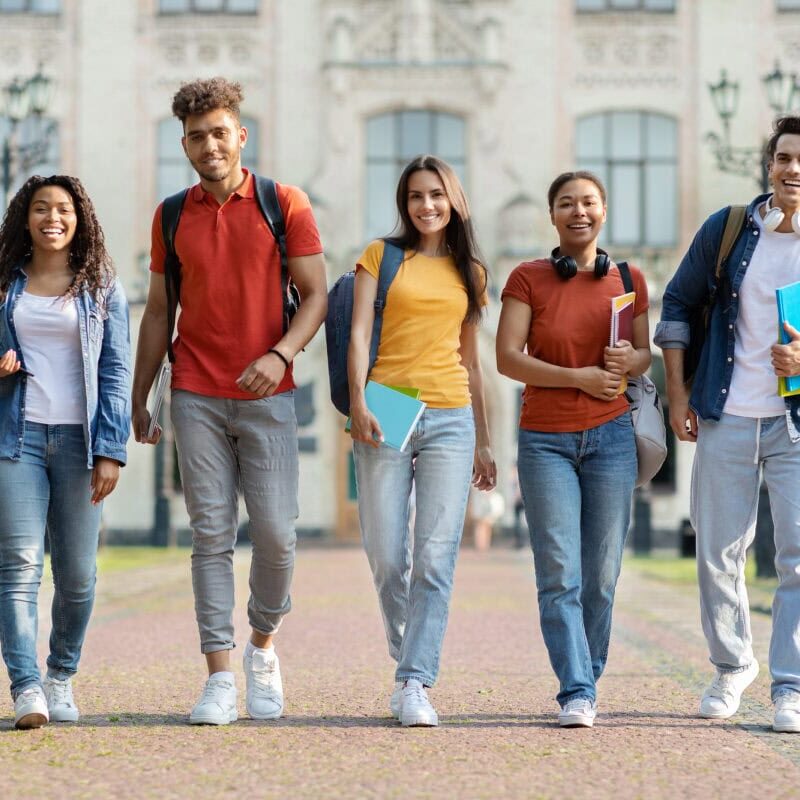 A group of smiling college students walking outside in front of a building