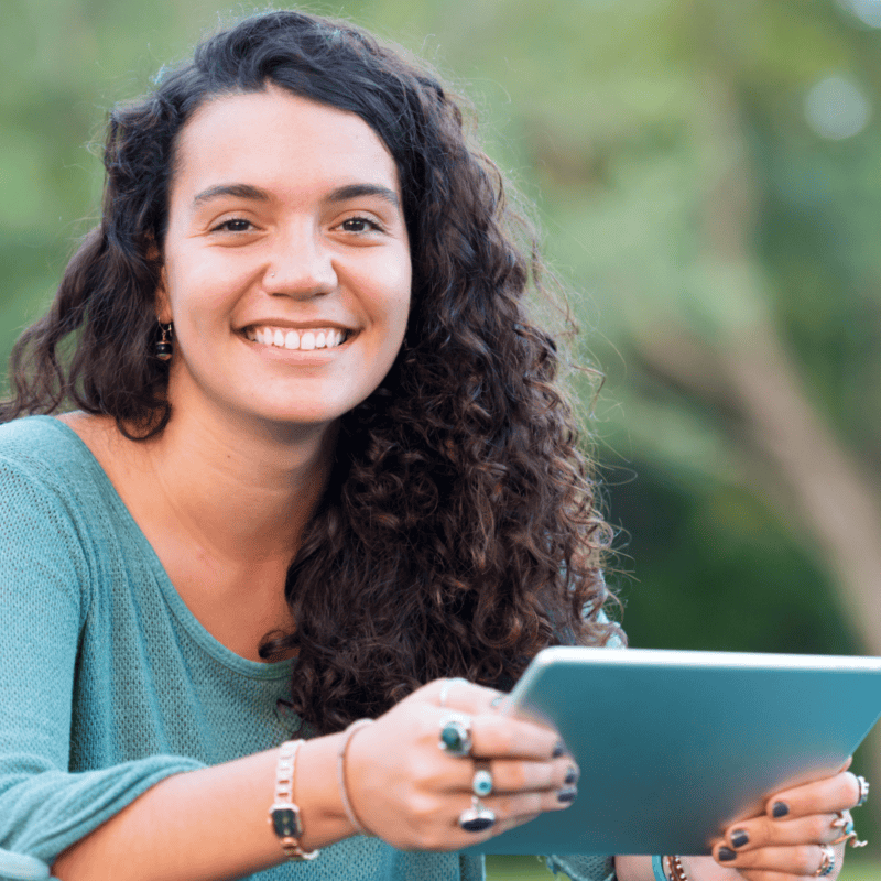 Smiling curly-haired college student sitting outside and holding a tablet