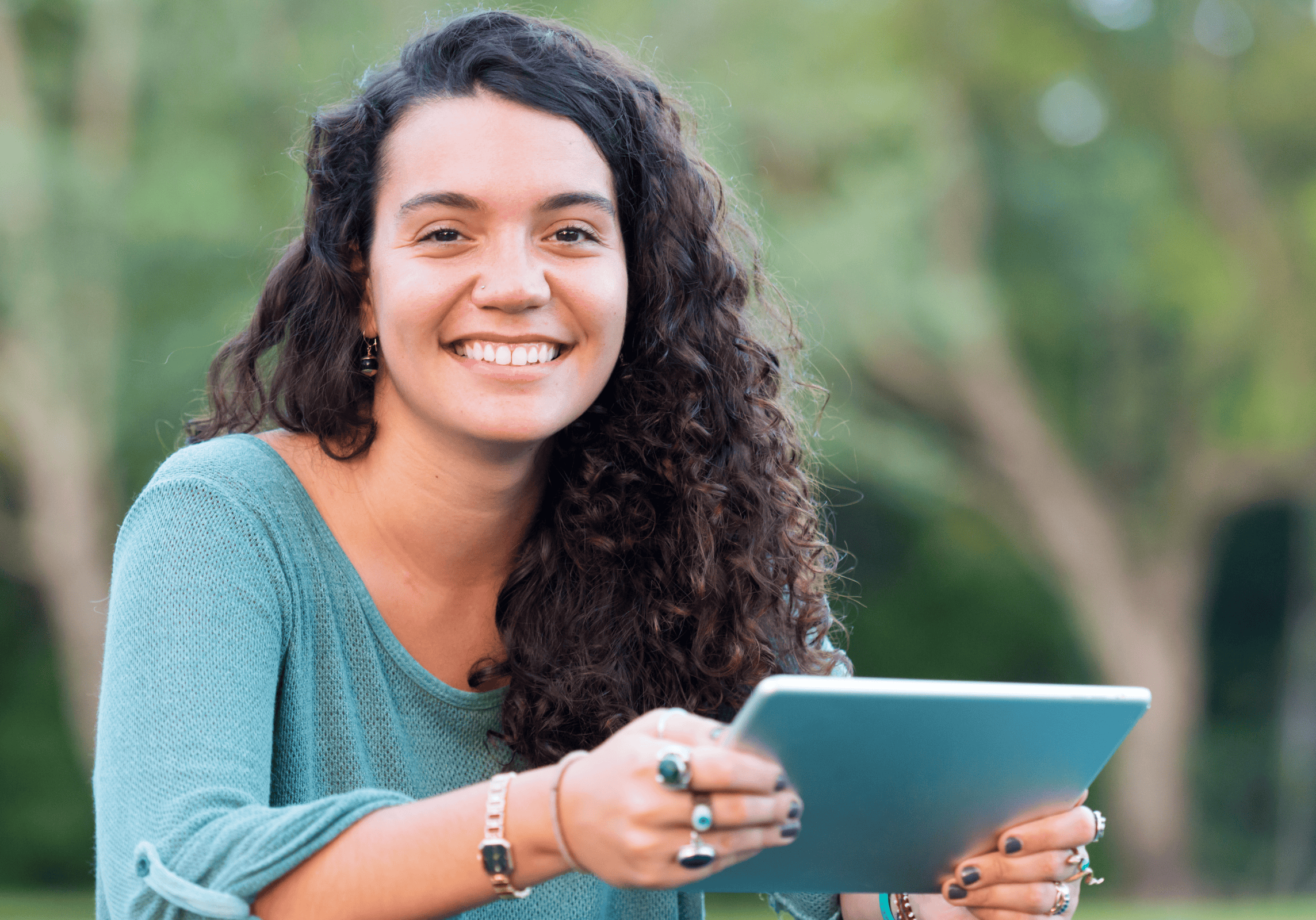 Smiling curly-haired college student sitting outside and holding a tablet