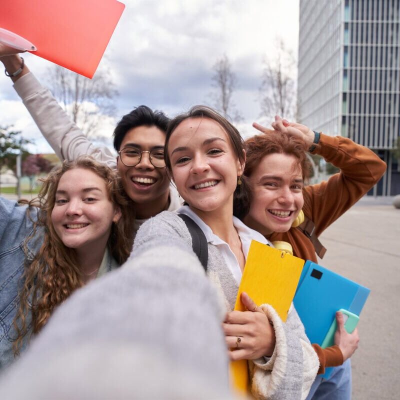 A diverse group of smiling college students taking a selfie outside