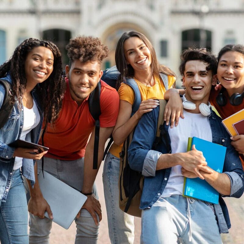 A diverse group of smiling college students outside with their backpacks and school books