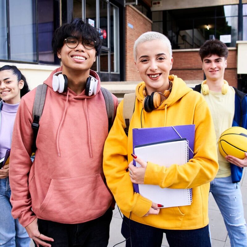 A group of gen Z classmate and friends looking at camera outdoors at campus of University.
