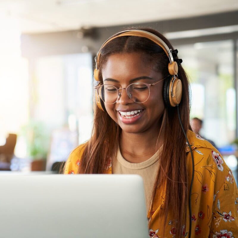 A smiling female college student wearing headphones and using a laptop