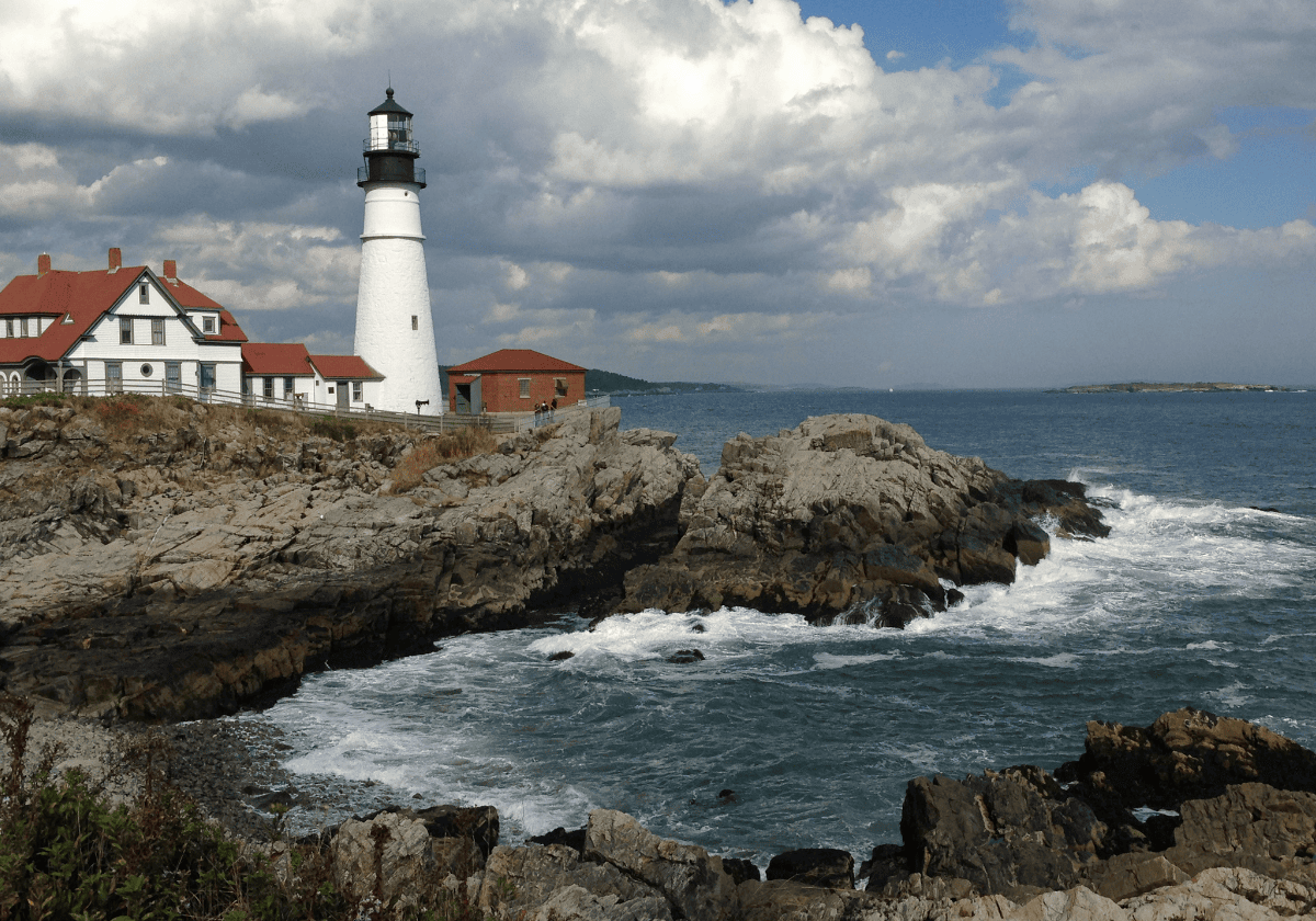 Lighthouse in New England - lighthouse on rocky cliffs by the ocean with a blue sky and clouds in the background