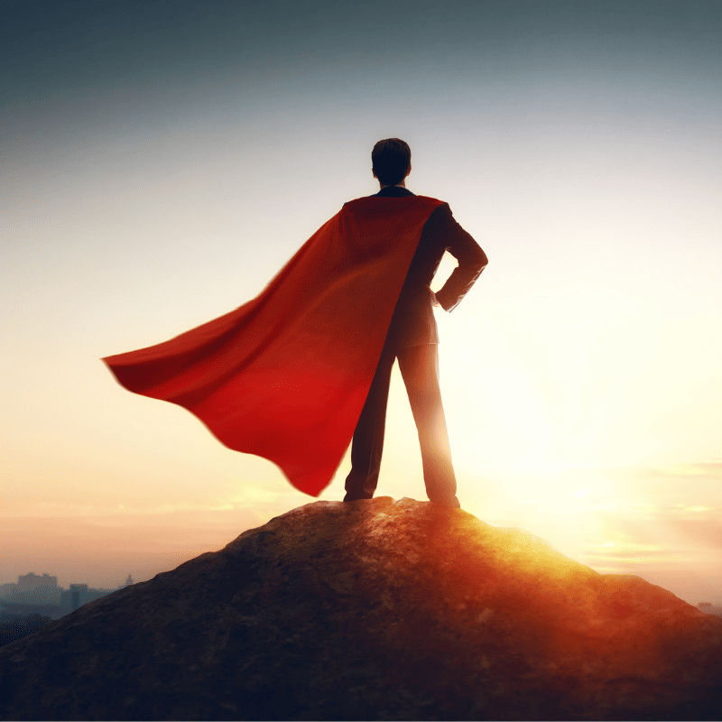A person standing on a hilltop wearing a red cape