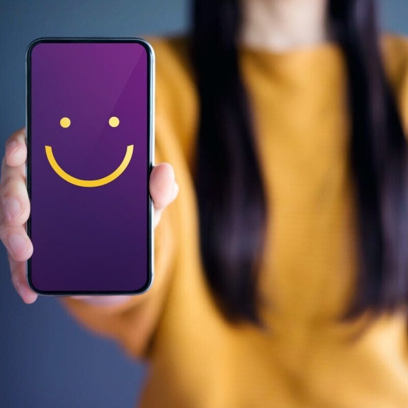 Woman holding a phone with a yellow smiley face on the screen