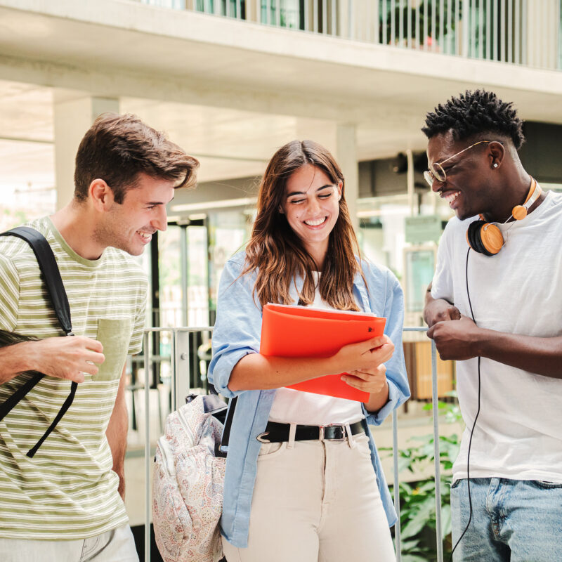 Three smiling college students standing together and looking at a folder