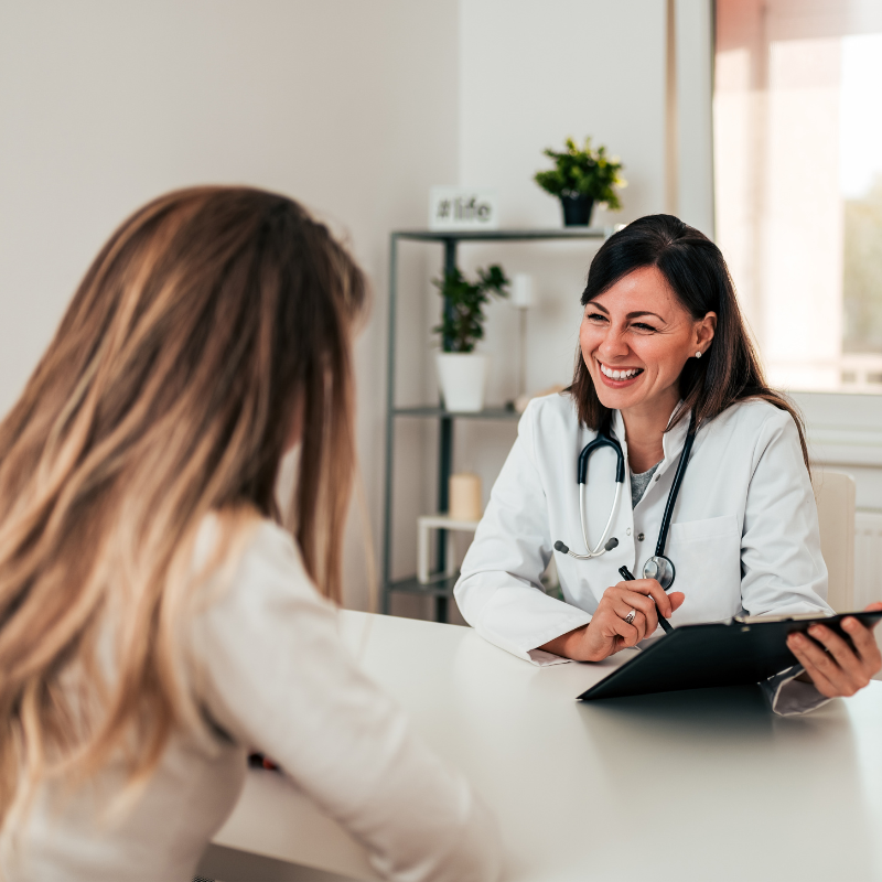A smiling doctor holding a clipboard and talking to patient