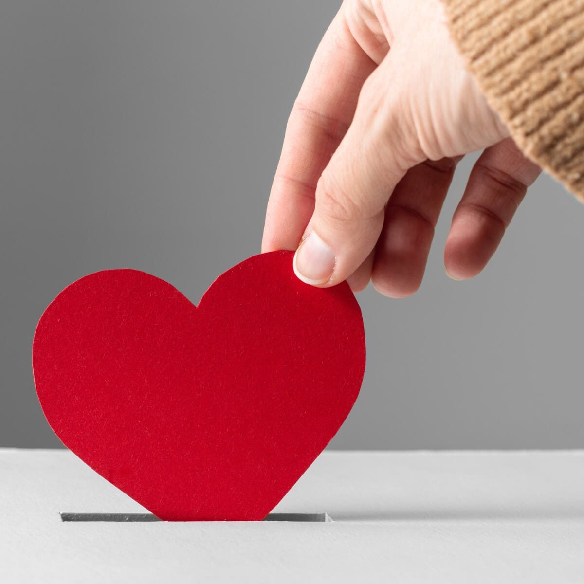 A hand inserting a red paper heart into a slot