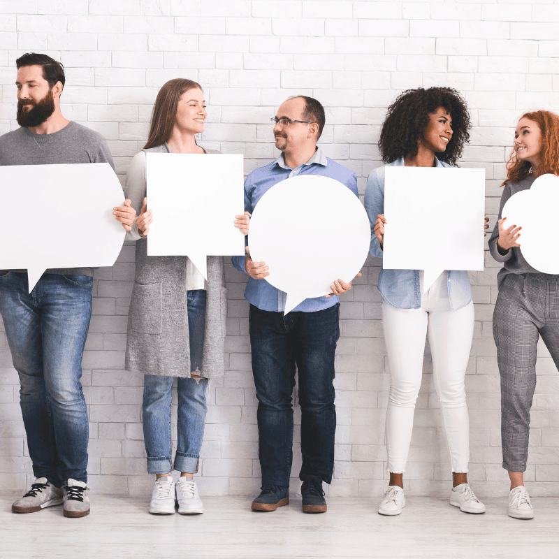 A group of individuals in front of a white brick wall holding white speech bubble cut outs