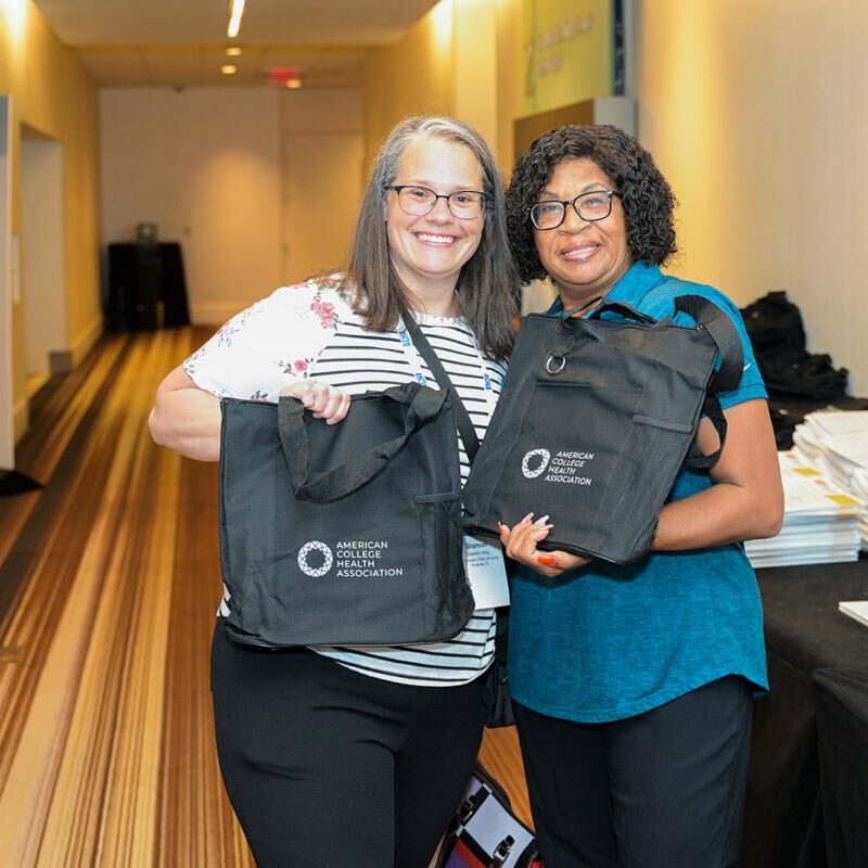 Two smiling conference attendees holding ACHA tote bags