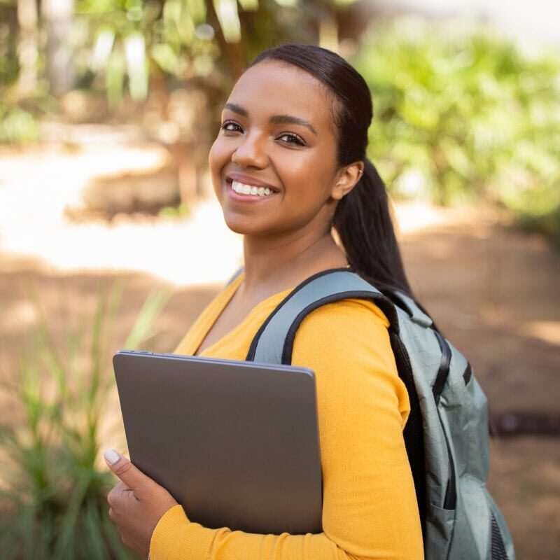 Portrait of happy student lady with laptop and backpack outdoors