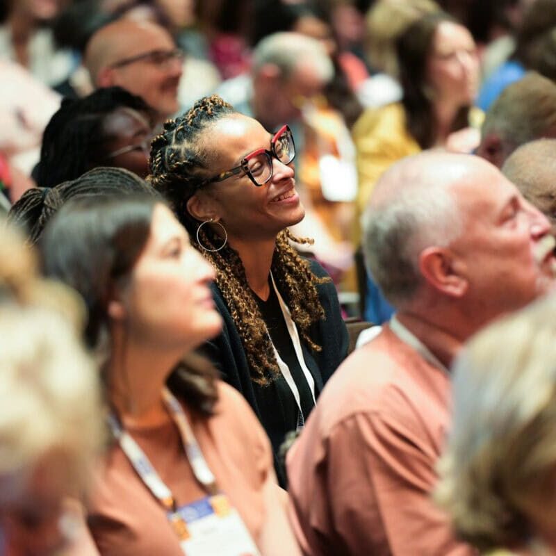 Smiling woman sitting in an audience of conference attendees.