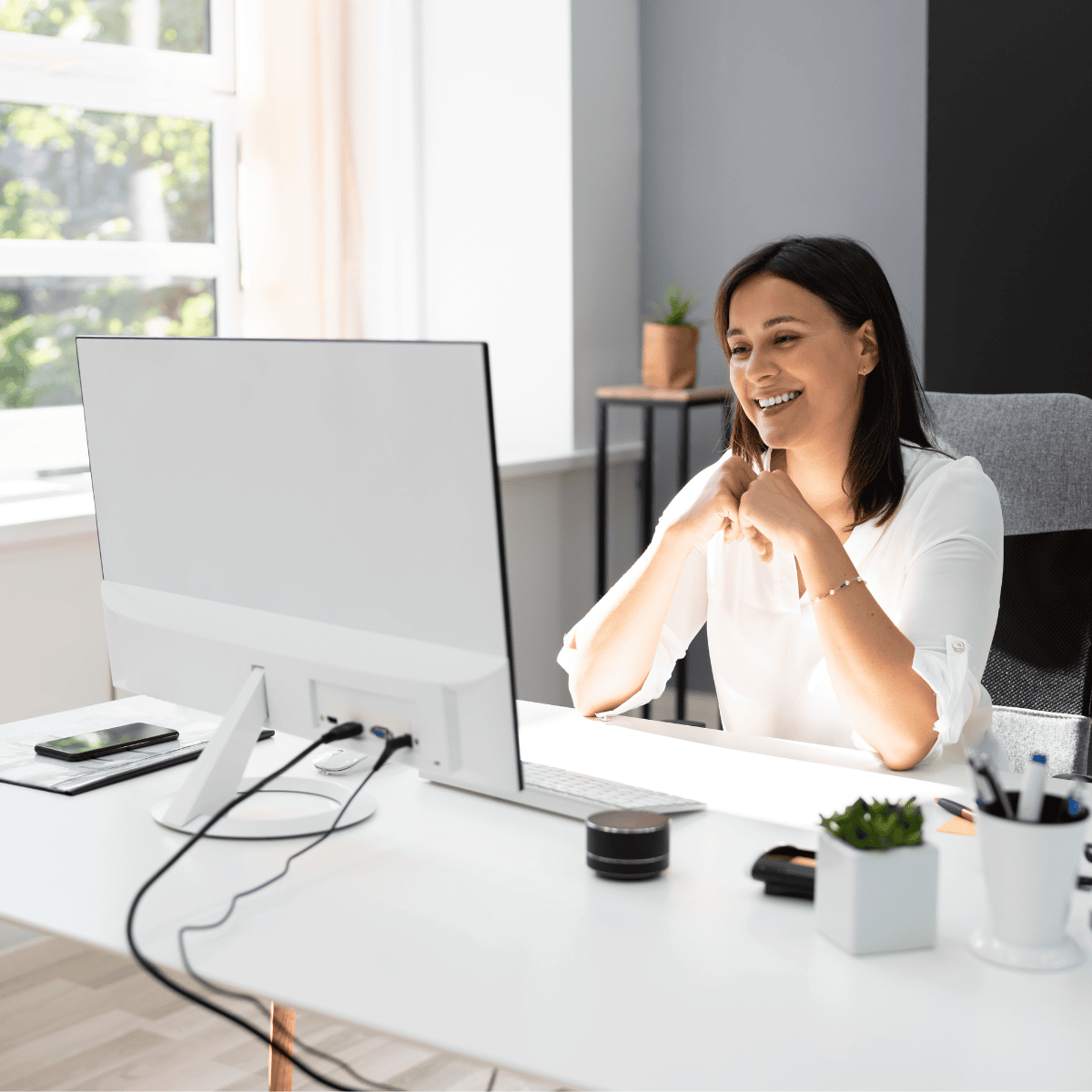 A smiling woman sitting at her desk in a virtual meeting on her computer