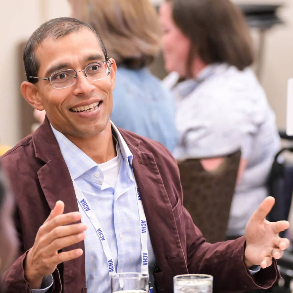 A man at the ACHA annual meeting smiling and talking to others at his table.